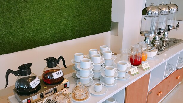 Disposição de buffet com dispensadores de café e chá, variedade de xícaras e pires, e seleção de doces.