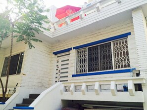 Un edificio blanco con detalles azules, un paraguas rojo y una escalera que lleva a un balcón.