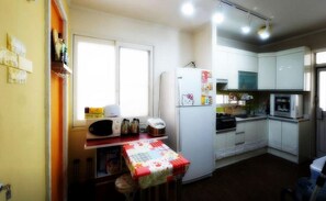 Una cocina compacta con armarios blancos, un microondas, un refrigerador con un adhesivo de Hello Kitty y una mesa pequeña con mantel floreado.