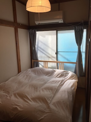 A bedroom with a bed, a window with curtains, and an air conditioning unit. - Star Inn Tokyo - Hostel (Tokyo)