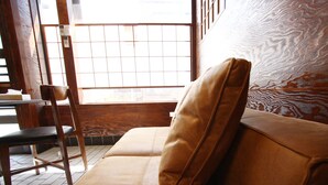 A room with a wooden floor, a brown sofa with a cushion, and a wooden chair. - Star Inn Tokyo - Hostel (Tokyo)