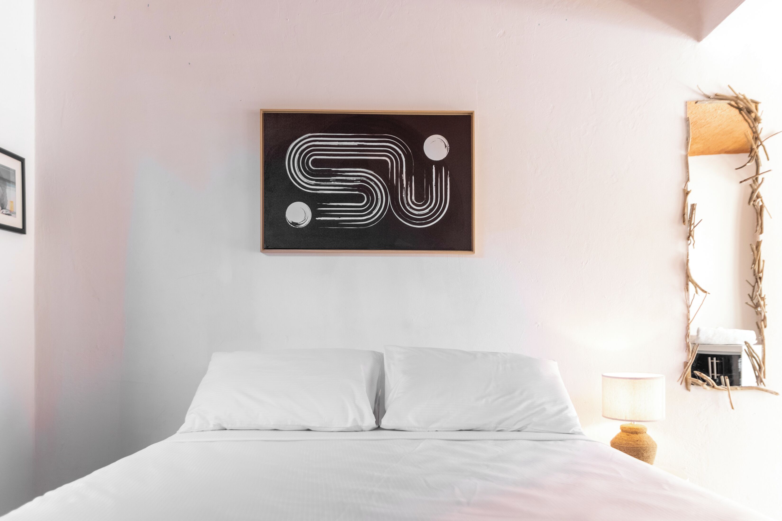 Un dormitorio con una cama, una obra de arte abstracta colgada en la pared, una lámpara de noche y un espejo también sujeto a la pared.