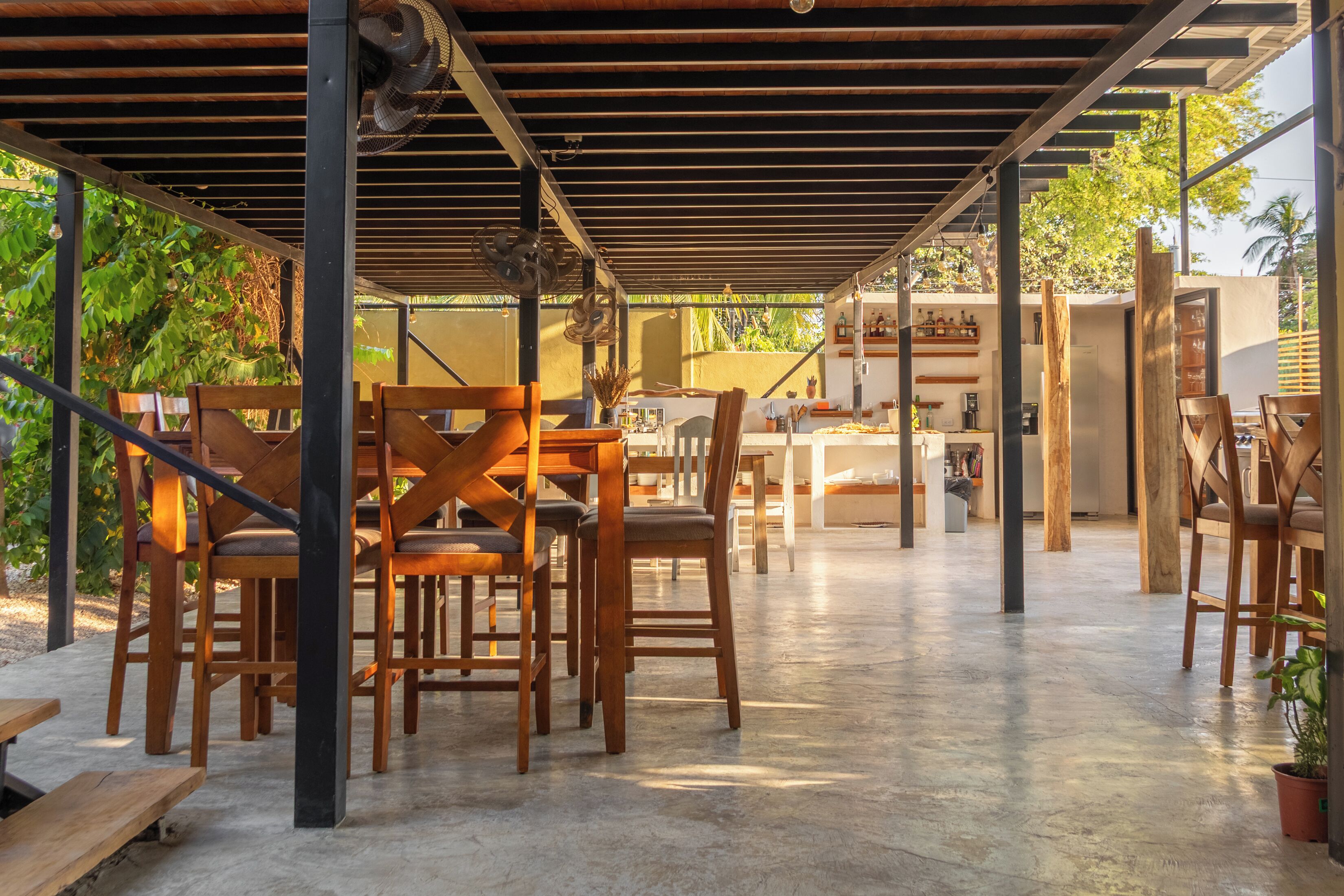 An outdoor covered patio with wooden furniture and a concrete floor.