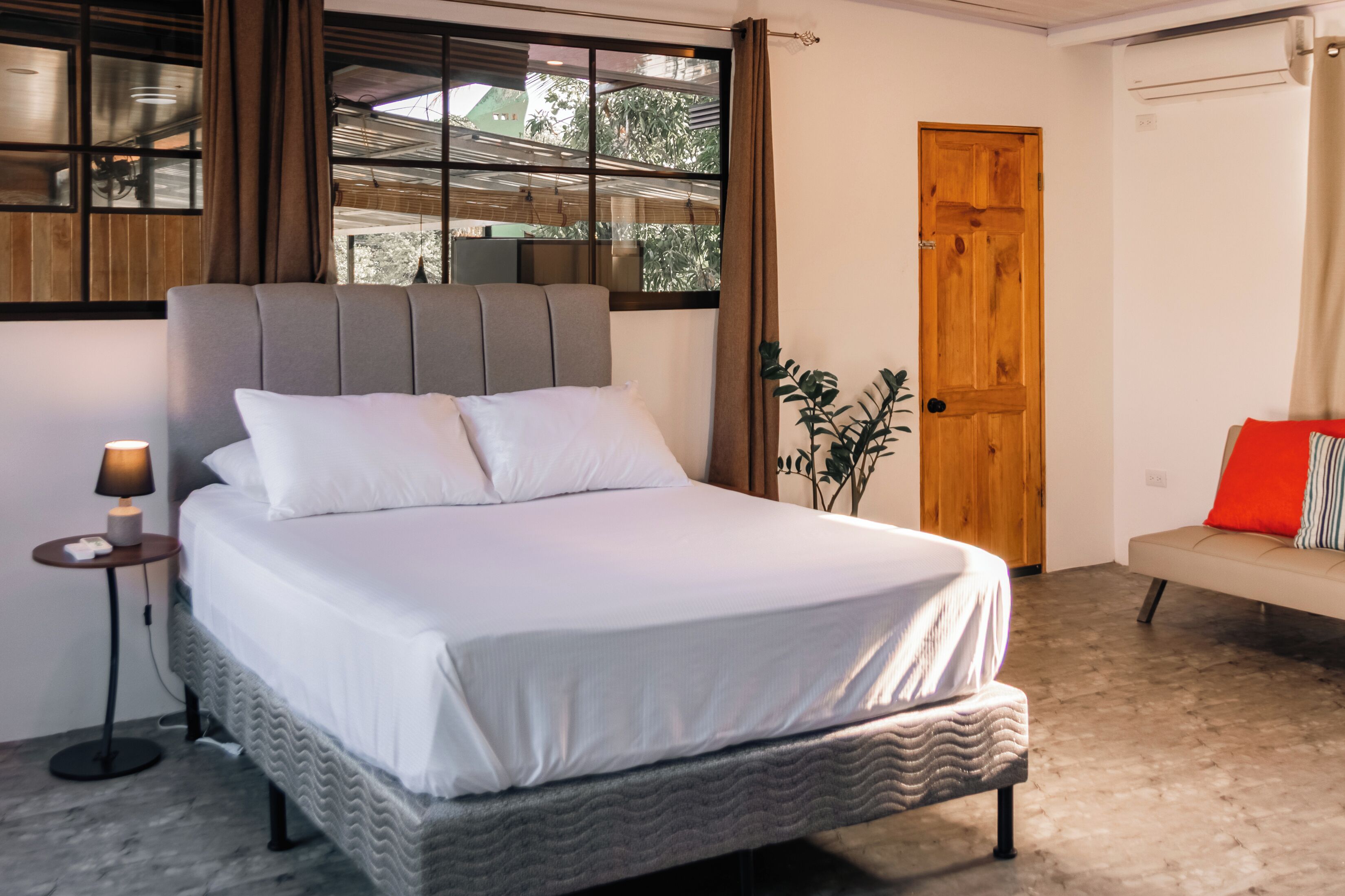 Une chambre à coucher avec un lit, une table de chevet, une lampe, une fenêtre et une porte.