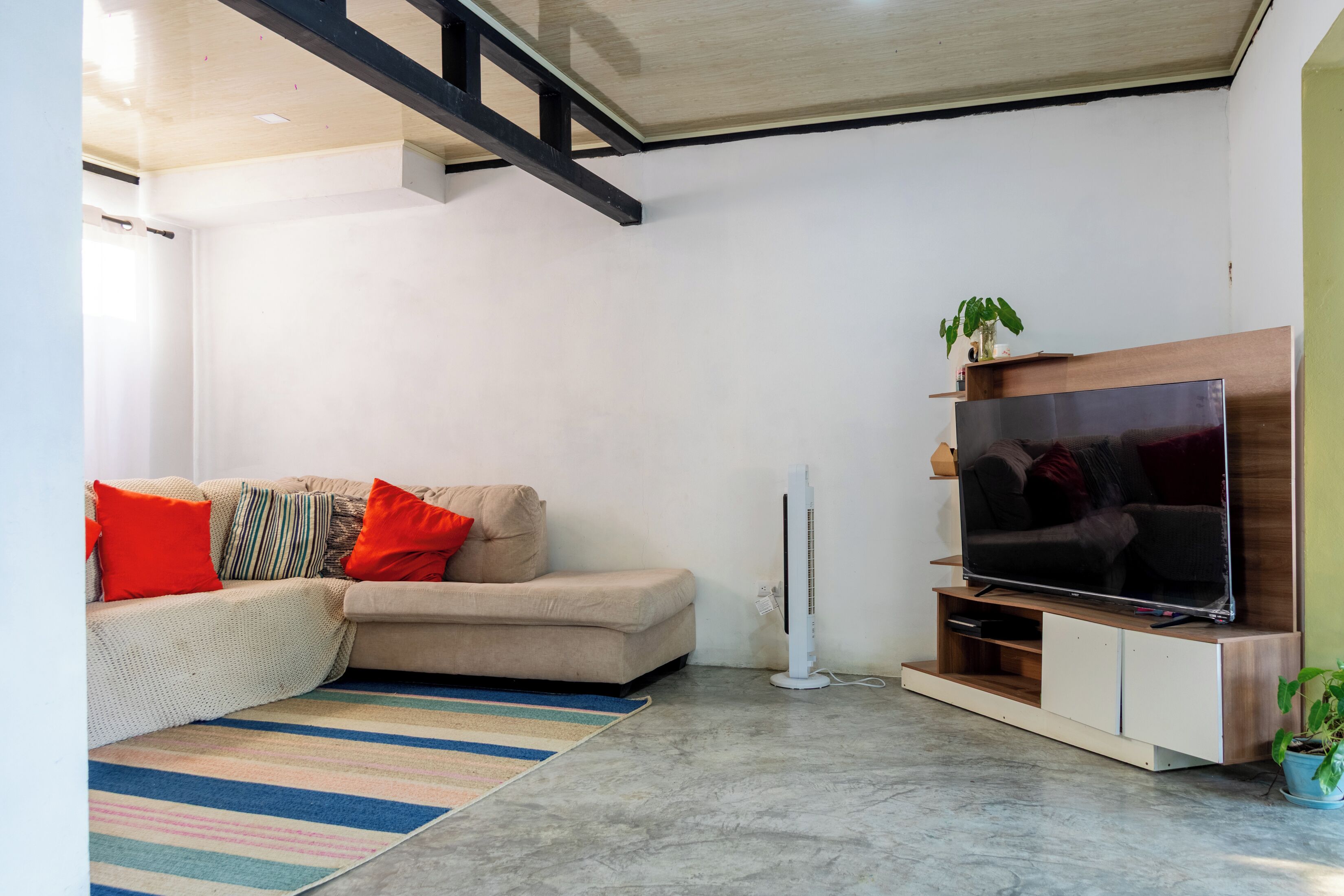 A modern living room with a sofa, a flat-screen TV, a fan, and a striped rug.