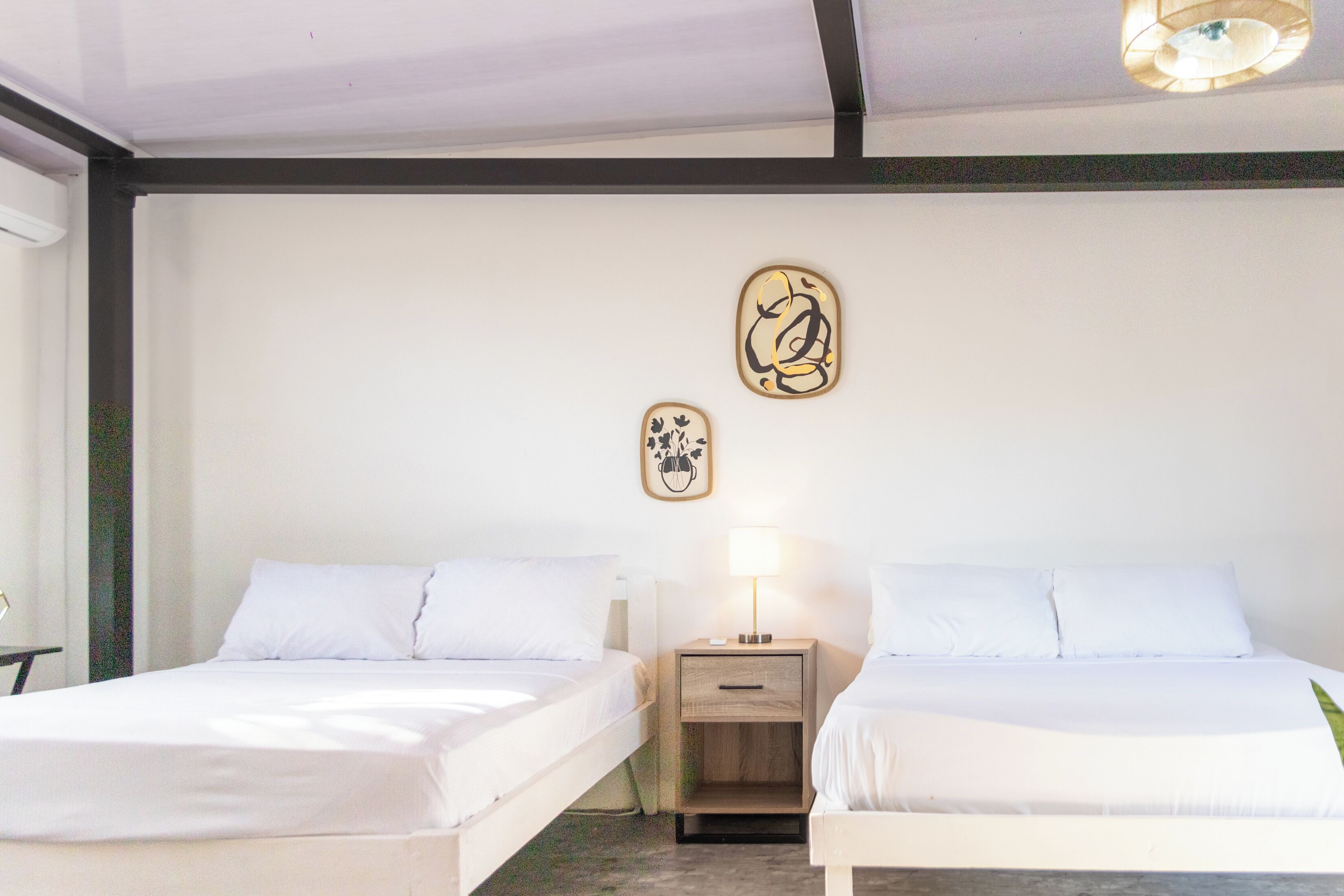 Habitación de hotel con dos camas, una mesita de noche con lámpara y una obra de arte en la pared.