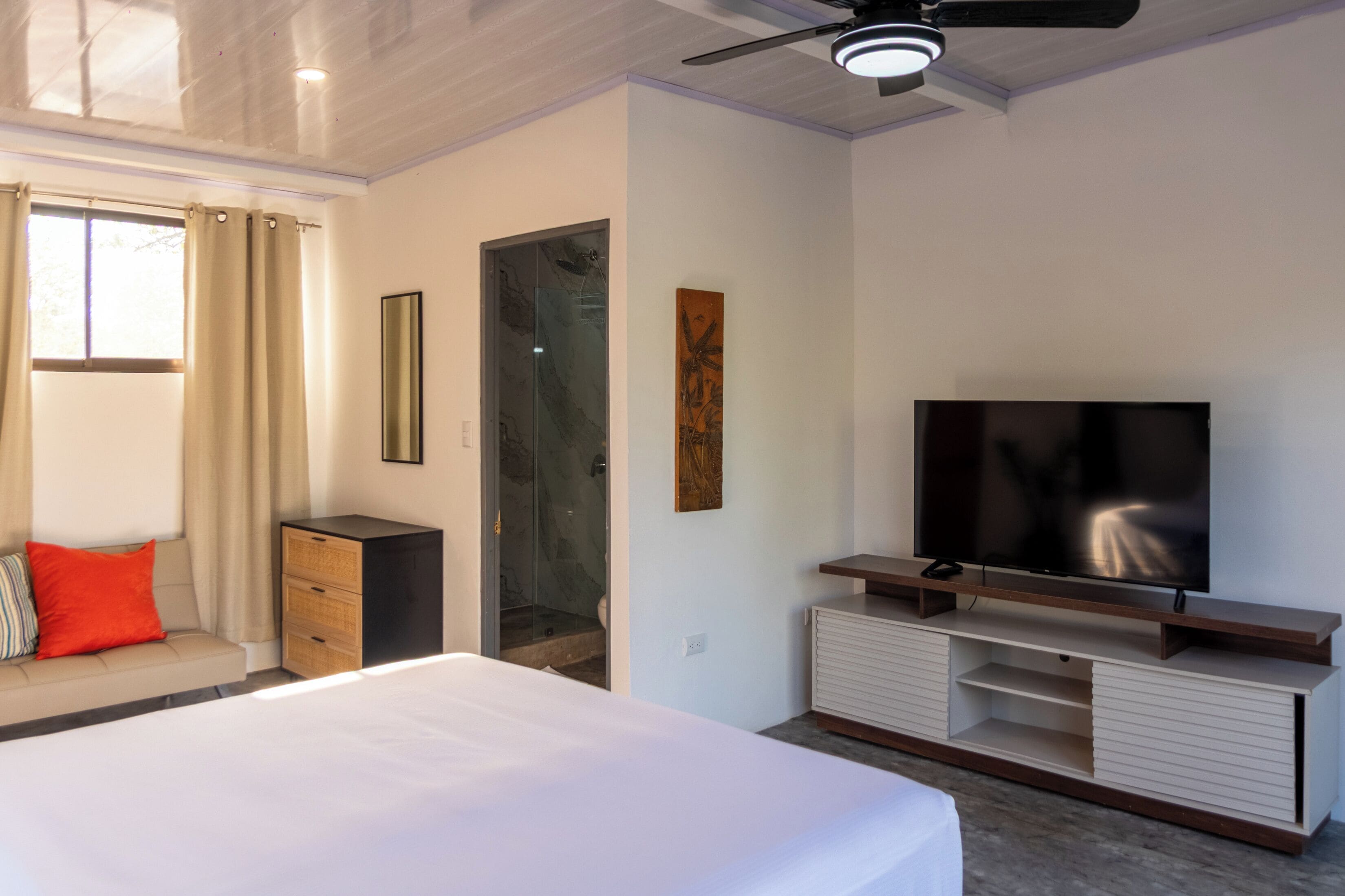 Een moderne hotelkamer met een bed, een televisie, een plafondventilator en een douche.