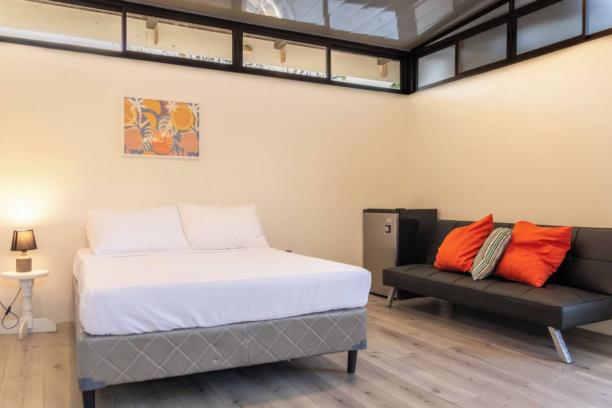 Un dormitorio con cama, sofá, mesita con lámpara, armario y ventana con persianas.