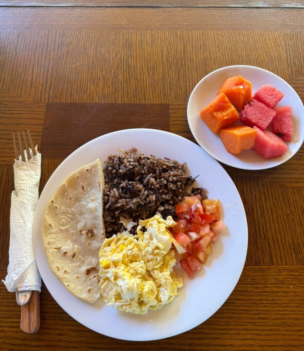 Un plato con arroz, huevos, tomates y una tortilla sobre una mesa de madera.