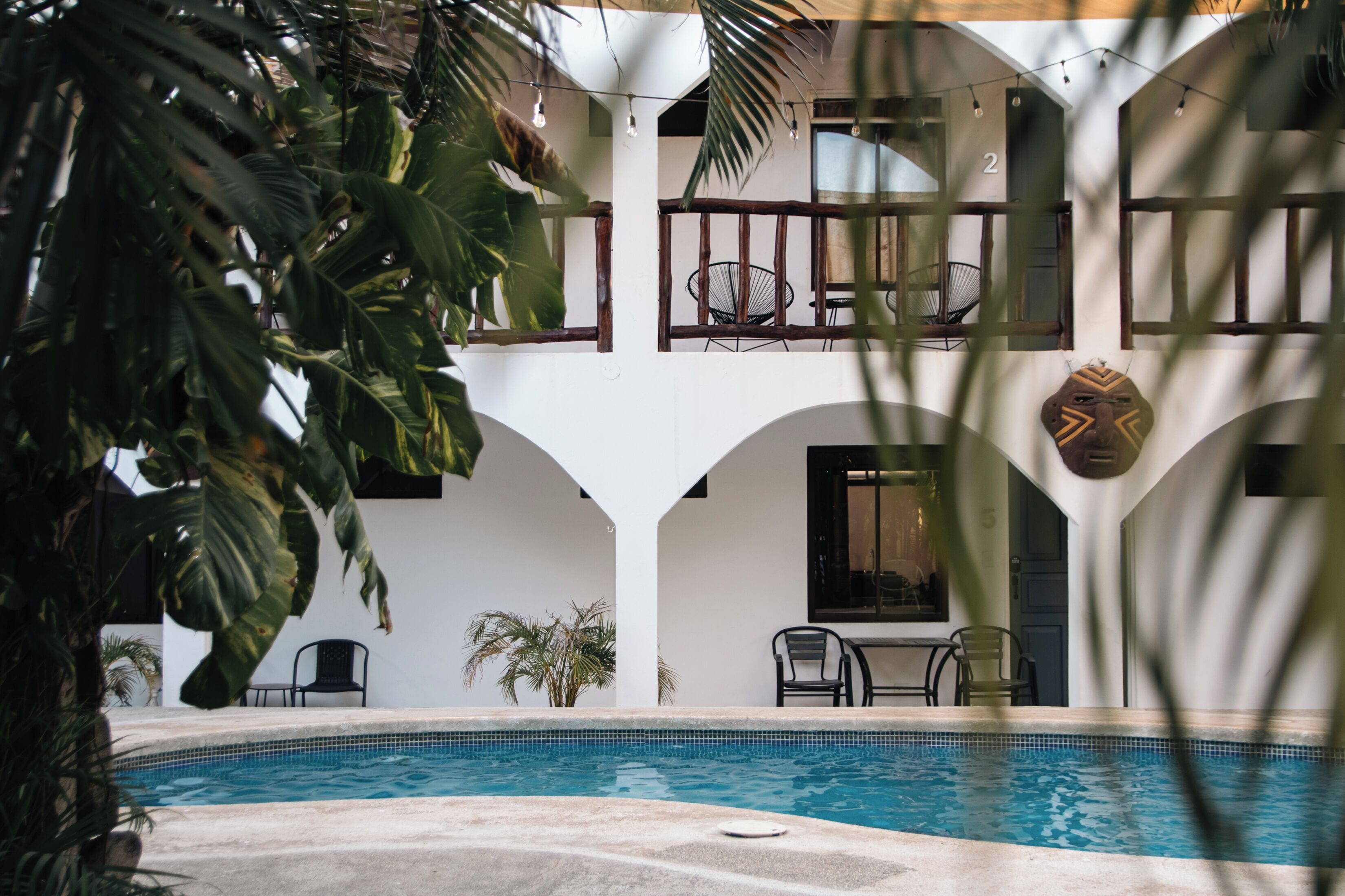 A pool area with a clear view of the pool, chairs, and a building with a white facade and arched windows.