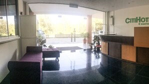 A hotel reception area with a reception desk, a seating area with a purple sofa, and a large window providing a view of the outdoors.