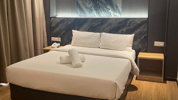 A modern hotel room with a large bed, wooden flooring, and a marble-patterned wall.