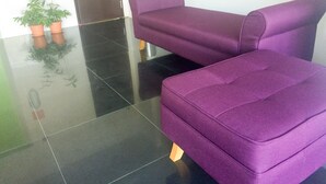 A purple sofa in a lobby with a tiled floor and potted plants.