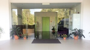 A modern building entrance with a glass door, potted plants, and a vehicle parked outside.