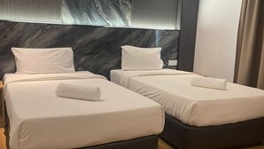 A hotel room with two beds, a marble headboard, wooden flooring, and a window with curtains.