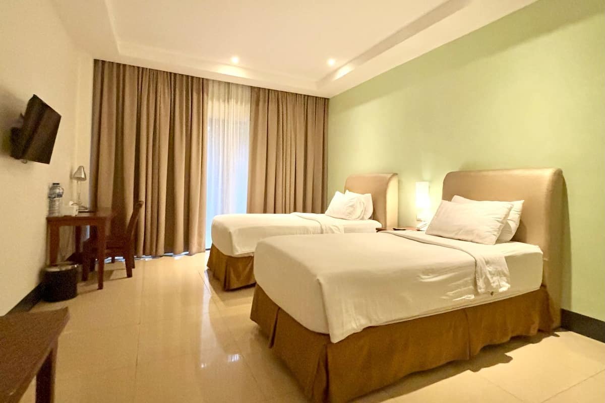 A hotel room with two beds, a desk, a chair, a TV, and a window with curtains.