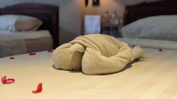 A neatly made bed with a towel folded in the center, a lamp in the background, and a nightstand with bottles.