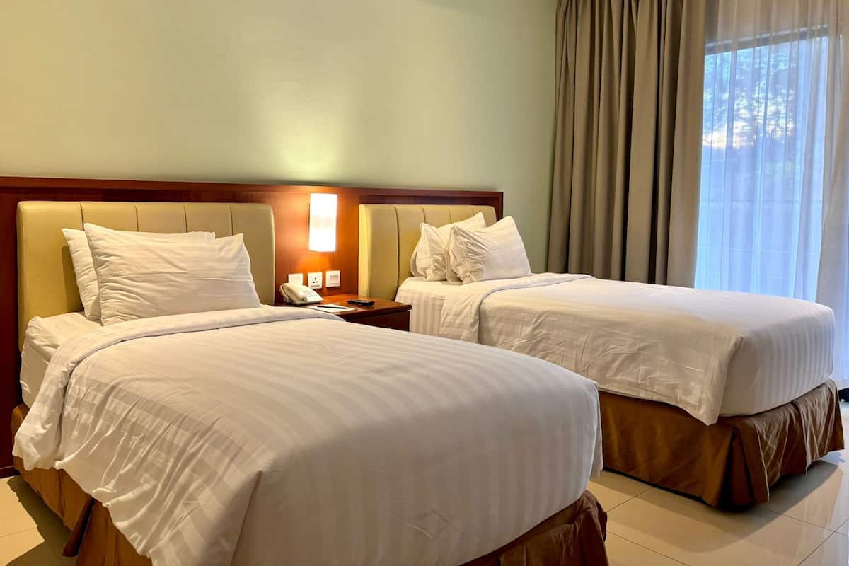 A hotel room with two beds, a nightstand with a phone, and a window with curtains.