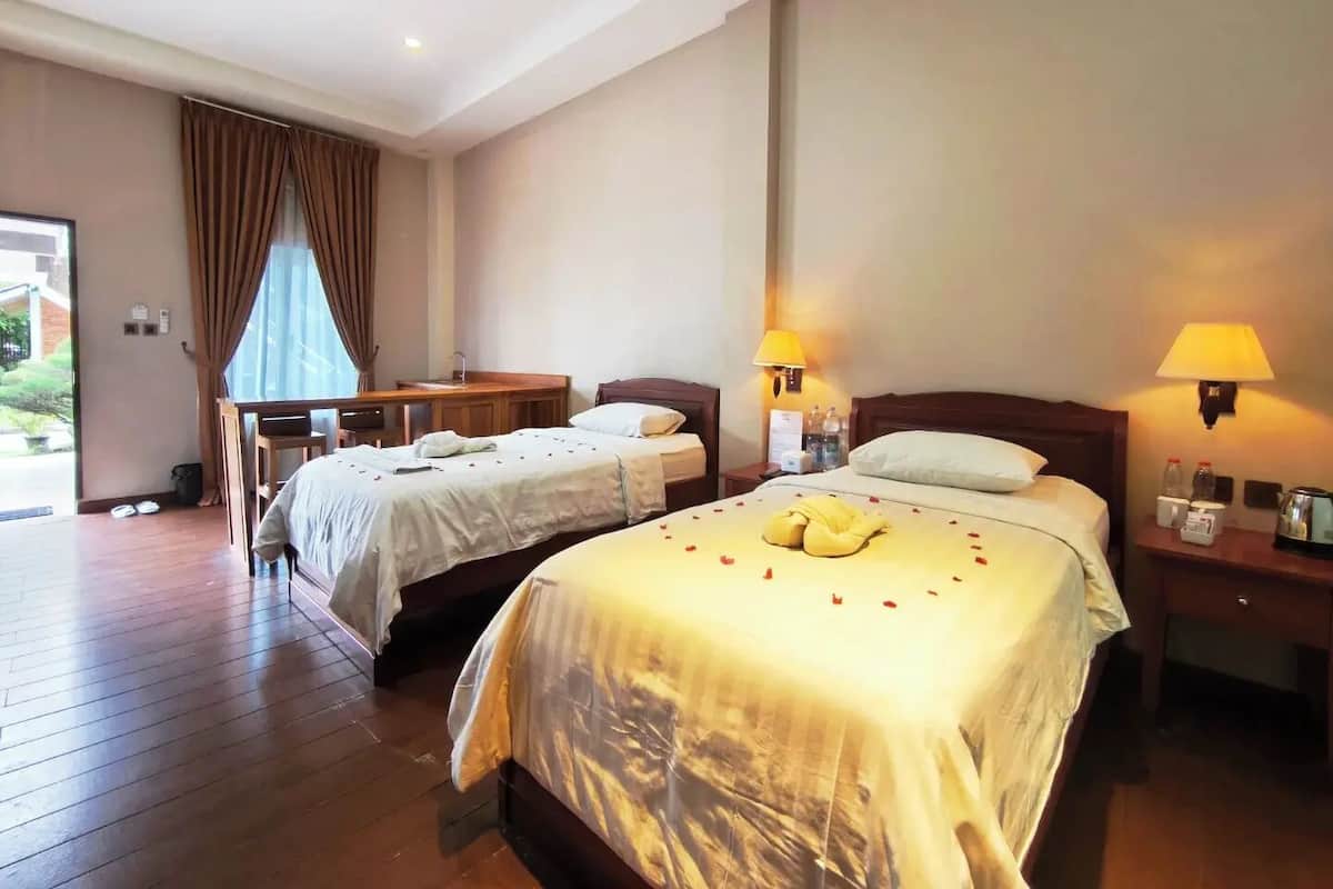 A hotel room with two beds, a desk, a chair, a small table, and a window with curtains.