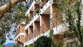 A multi-story building with a brick facade, balconies, and surrounding greenery.