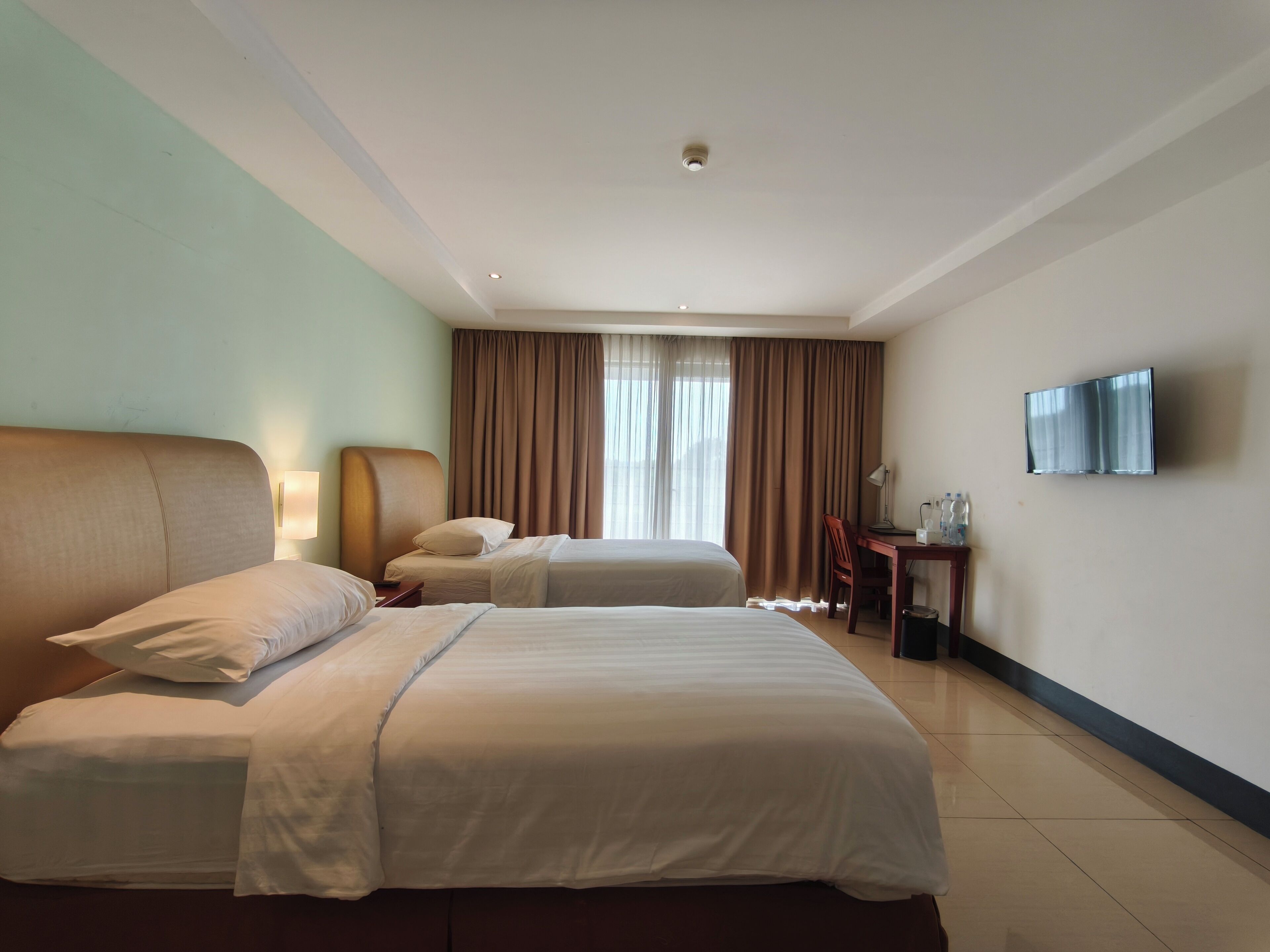 A hotel room with two beds, a desk, a chair, a TV, and a window with curtains.