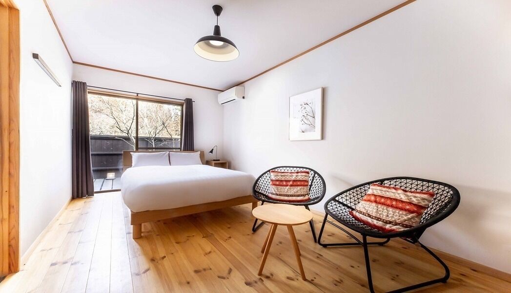 Quarto com cama, duas cadeiras, janela e luminária no teto.