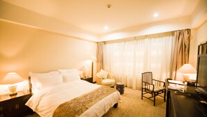 Quarto de hotel com uma cama grande, duas mesas de cabeceira com abajures, uma escrivaninha com cadeira e uma televisão.