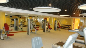 Uma academia com diversos aparelhos de exercício, espelhos e um suporte para sapatos.
