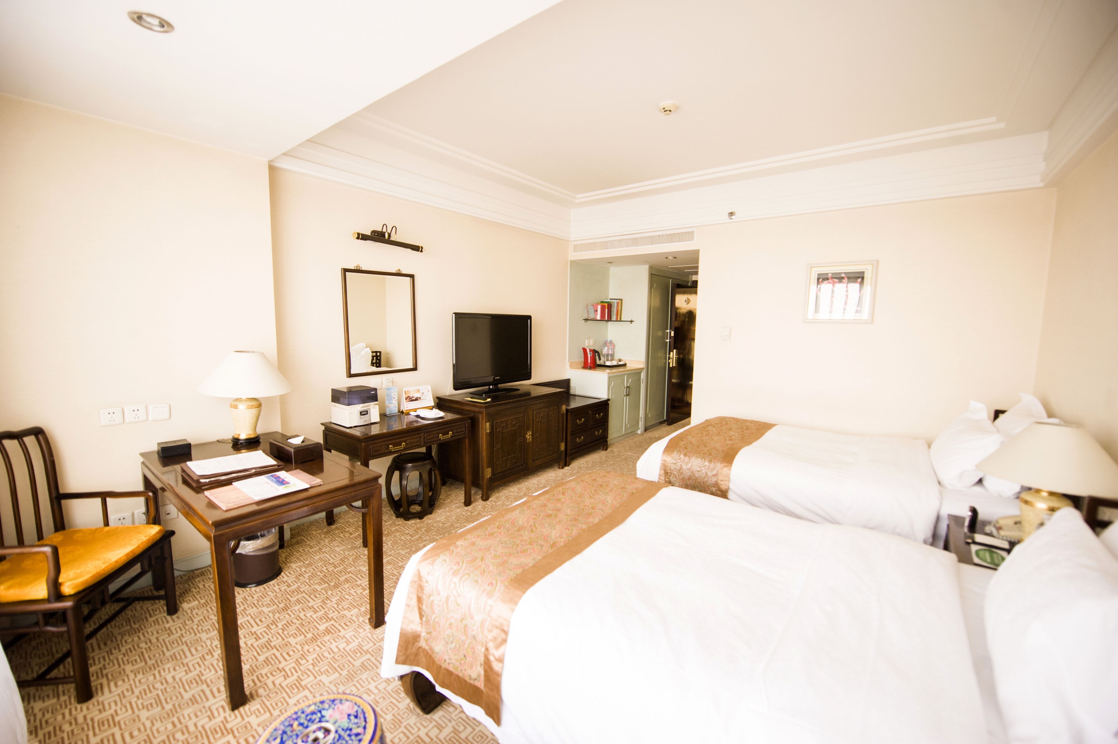 A hotel room with two beds, a desk with a computer, a chair, a television, and a wardrobe.