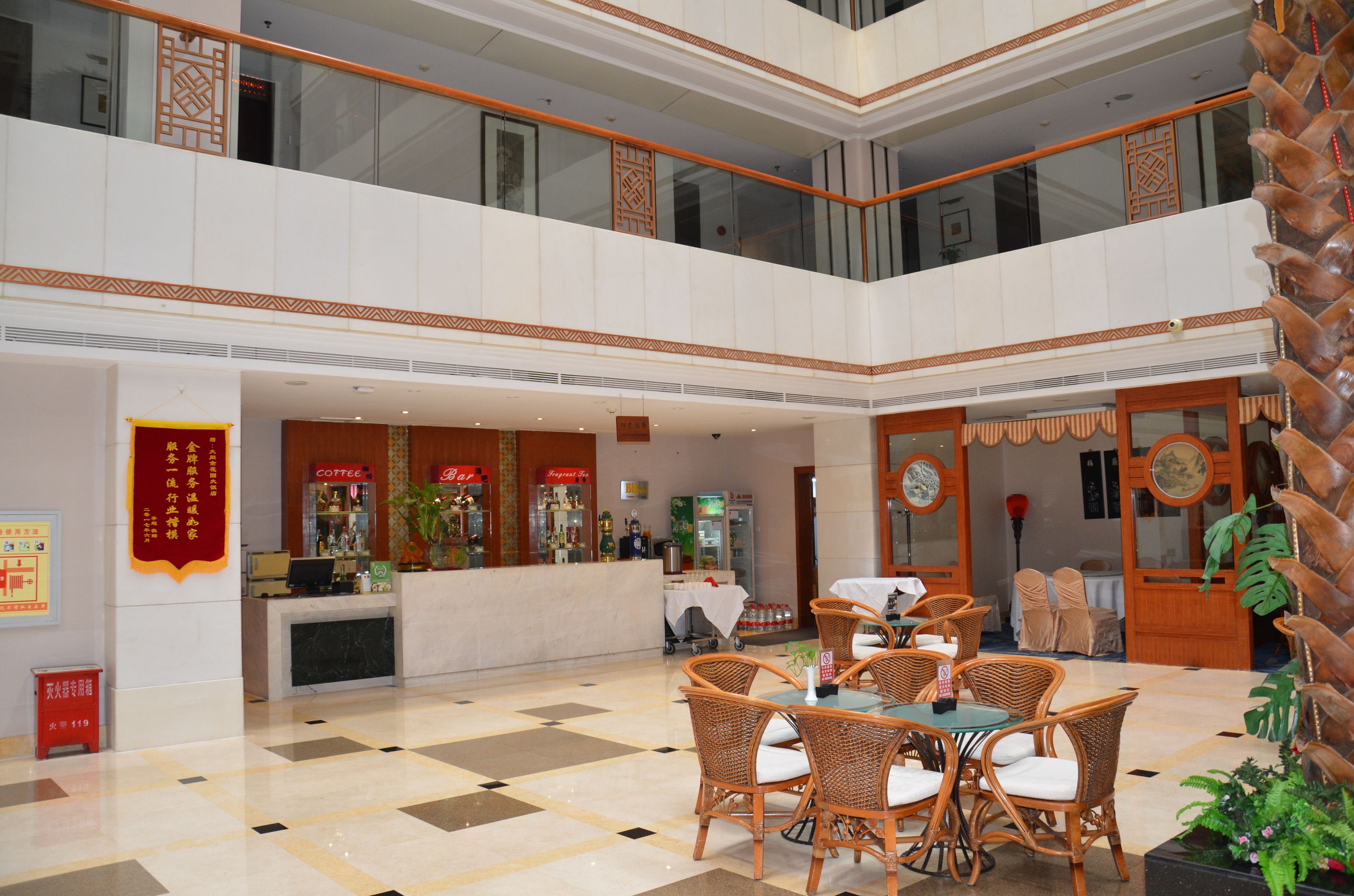 A hotel lobby with a check-in counter, a coffee shop, and a dining area with wicker furniture.