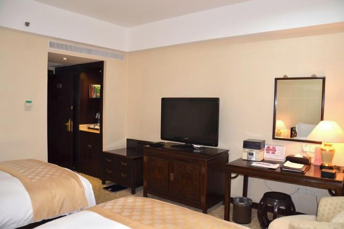 A hotel room with two beds, a desk with a television, a mirror, and a small table with a lamp.