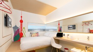 Habitación de hotel moderna con cama, escritorio y ordenador portátil, una ventana grande con vista a la ciudad y un baño con lavabo y espejo.