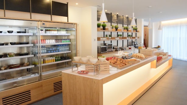 Una barra de desayuno moderna con bebidas refrigeradas, estantes con condimentos y una variedad de alimentos para el desayuno.