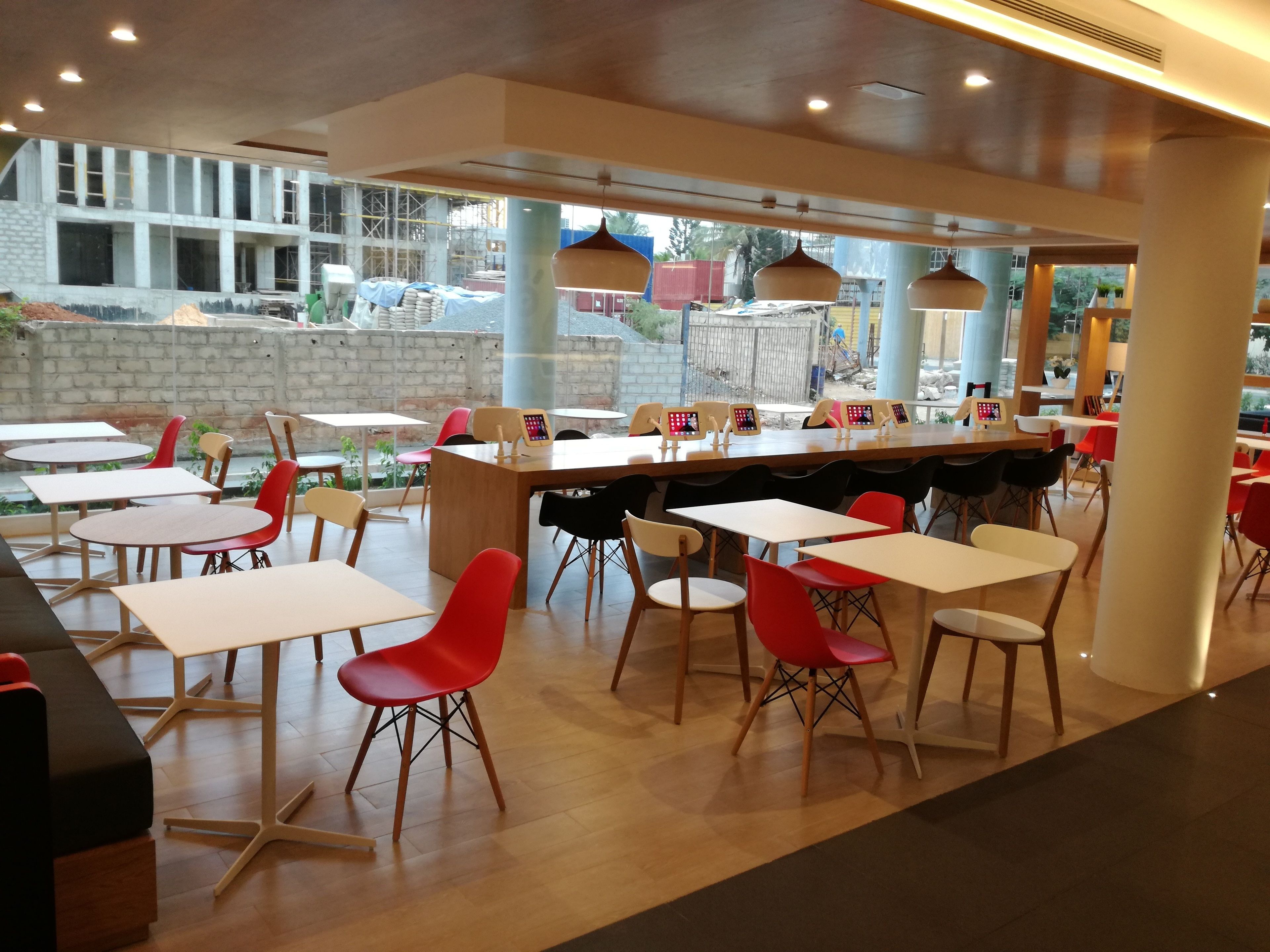 A modern restaurant with a mix of red and black chairs, wooden tables, and pendant lighting.