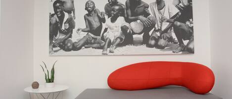A room with a large black and white photograph on the wall, a small white table with a plant, and a red bean bag chair.