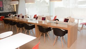 Una sala de conferencias moderna con una larga mesa, sillas negras y rojas, e iluminación colgante.