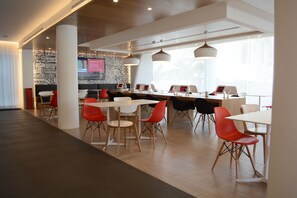 A modern dining area with white tables and red chairs, large windows, and a patterned wall in the background. - Yaas Hotel Dakar Almadies (Dakar)