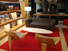 Un área de descanso moderna con un sofá gris, sillas de madera y una mesa blanca.