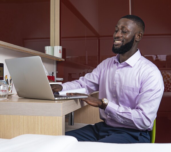 A man sitting at a desk with a laptop, wearing a watch and a purple shirt.