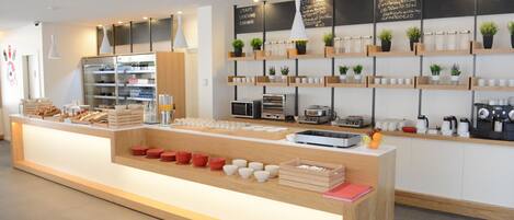 A modern cafe with a central counter, shelves with plants, and a chalkboard menu.