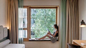 A room with a large window, a sofa, a desk, and a chair. - Hotel the YARD Berlin (Berlin)