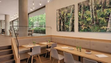 A modern restaurant with a wooden bench seating area, a staircase, and large forest-themed paintings on the wall.