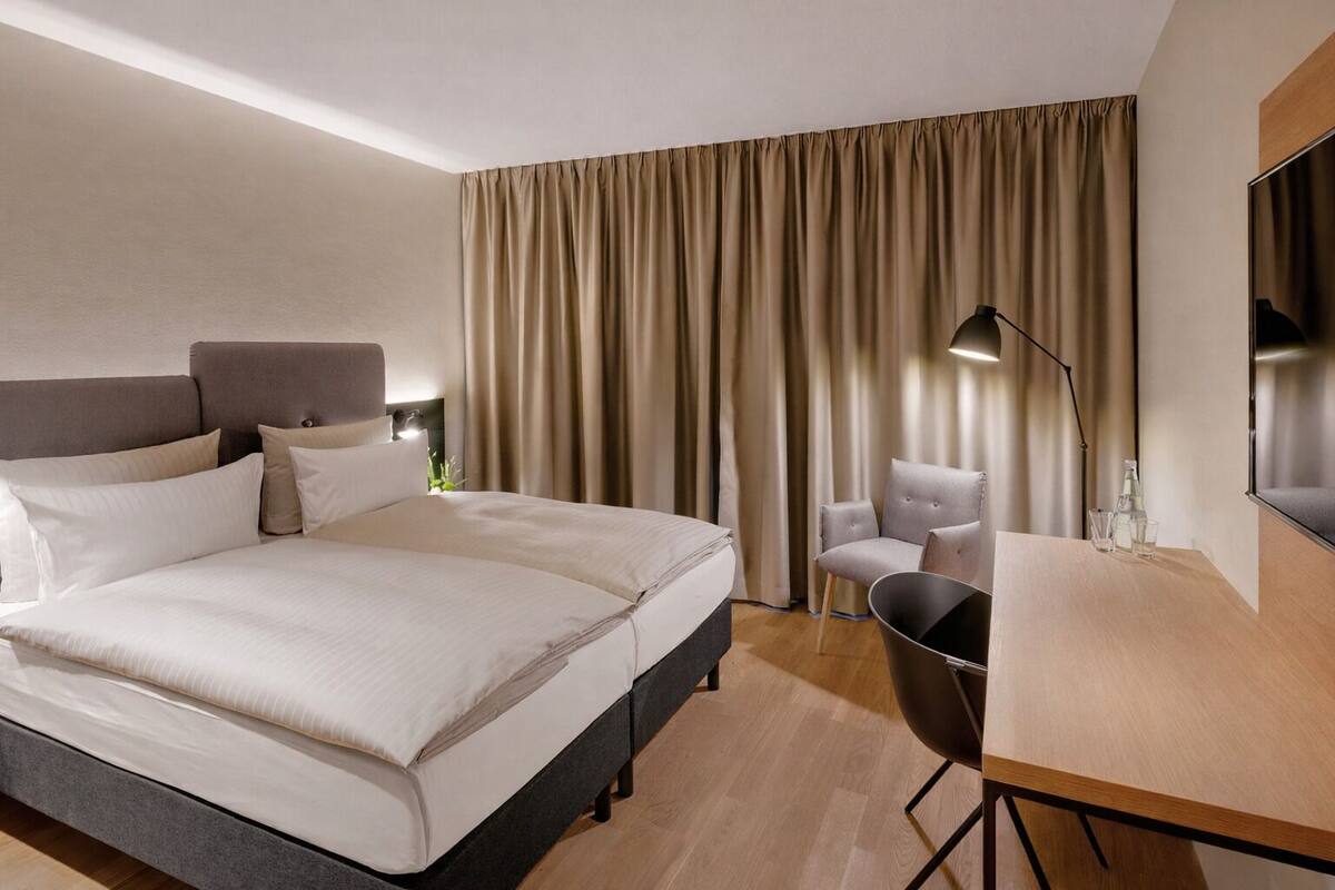 A hotel room with a bed, a desk, a chair, and a TV.