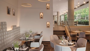 A modern restaurant interior with round tables, comfortable seating, and framed wine bottles on the wall. - Hotel the YARD Berlin (Berlin)