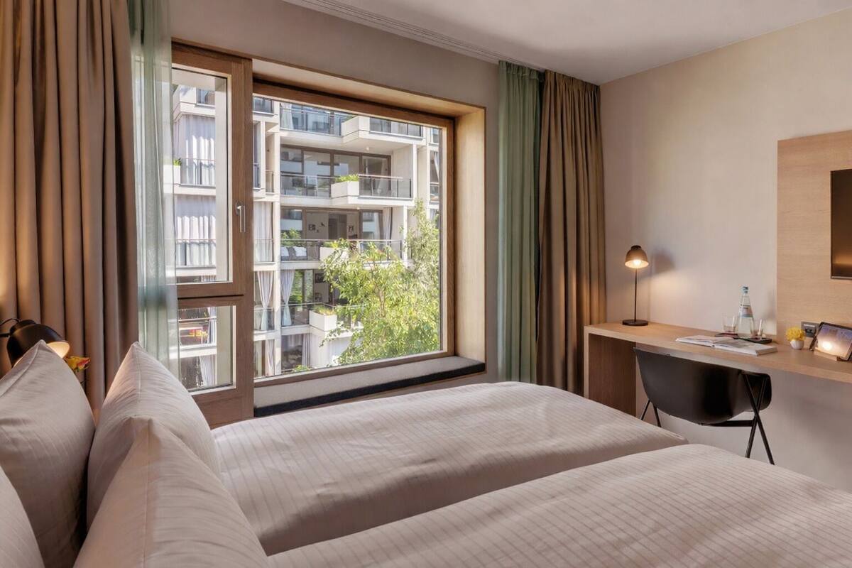 A hotel room with a large window, a desk, and a bed.