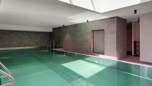 A modern indoor swimming pool with clear glass walls, a metal ladder, and a skylight. - Hotel the YARD Berlin (Berlin)