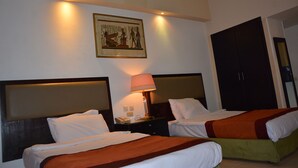 Habitación de hotel con dos camas, una mesita de noche con lámpara y un cuadro colgado en la pared.