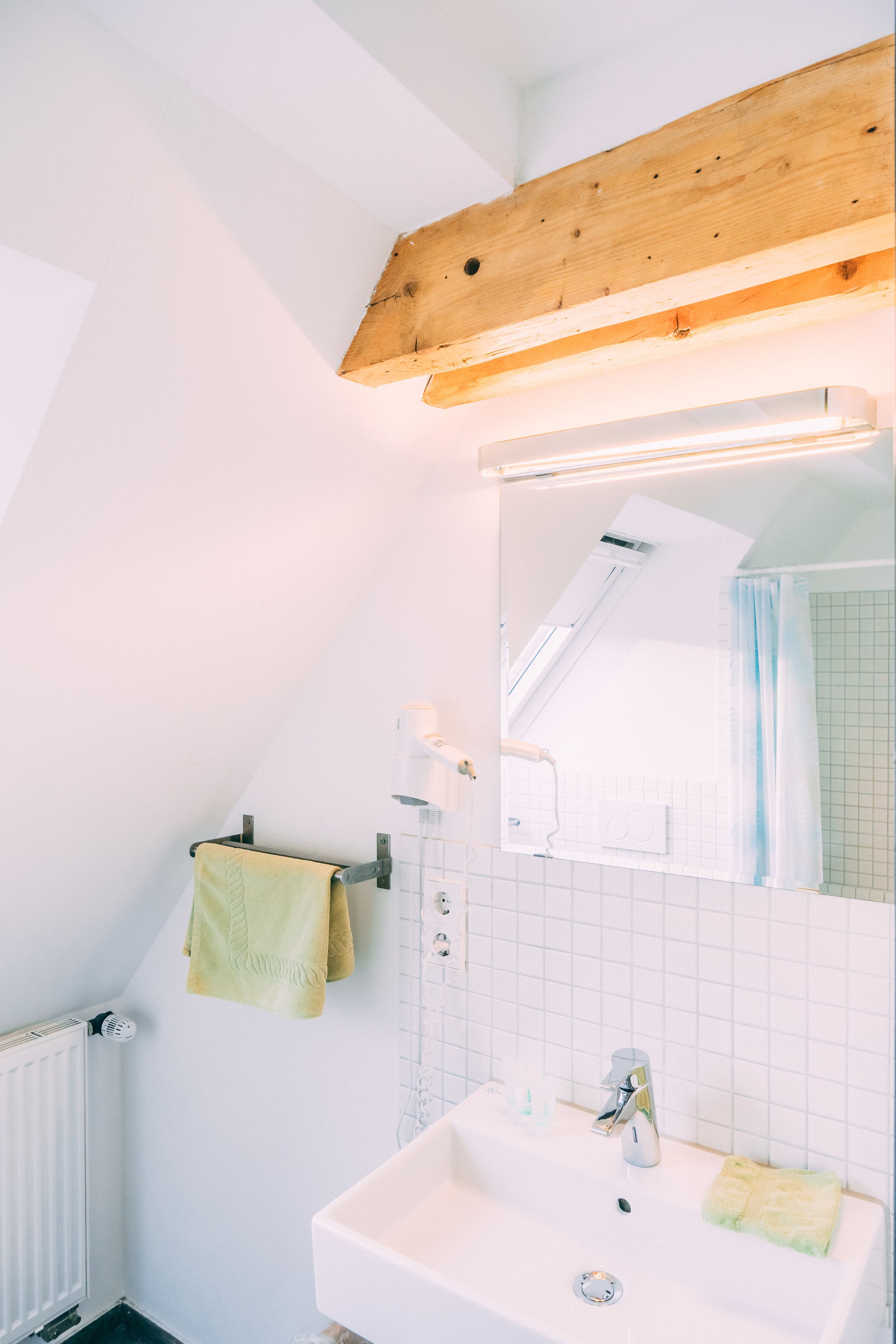 A bathroom with a white sink, a mirror, a towel rack, and a wooden ceiling beam.