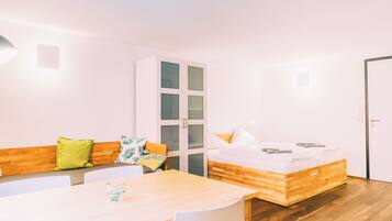 A modern room with a wooden bed, a white sofa with cushions, a dining table, and a glass of water.