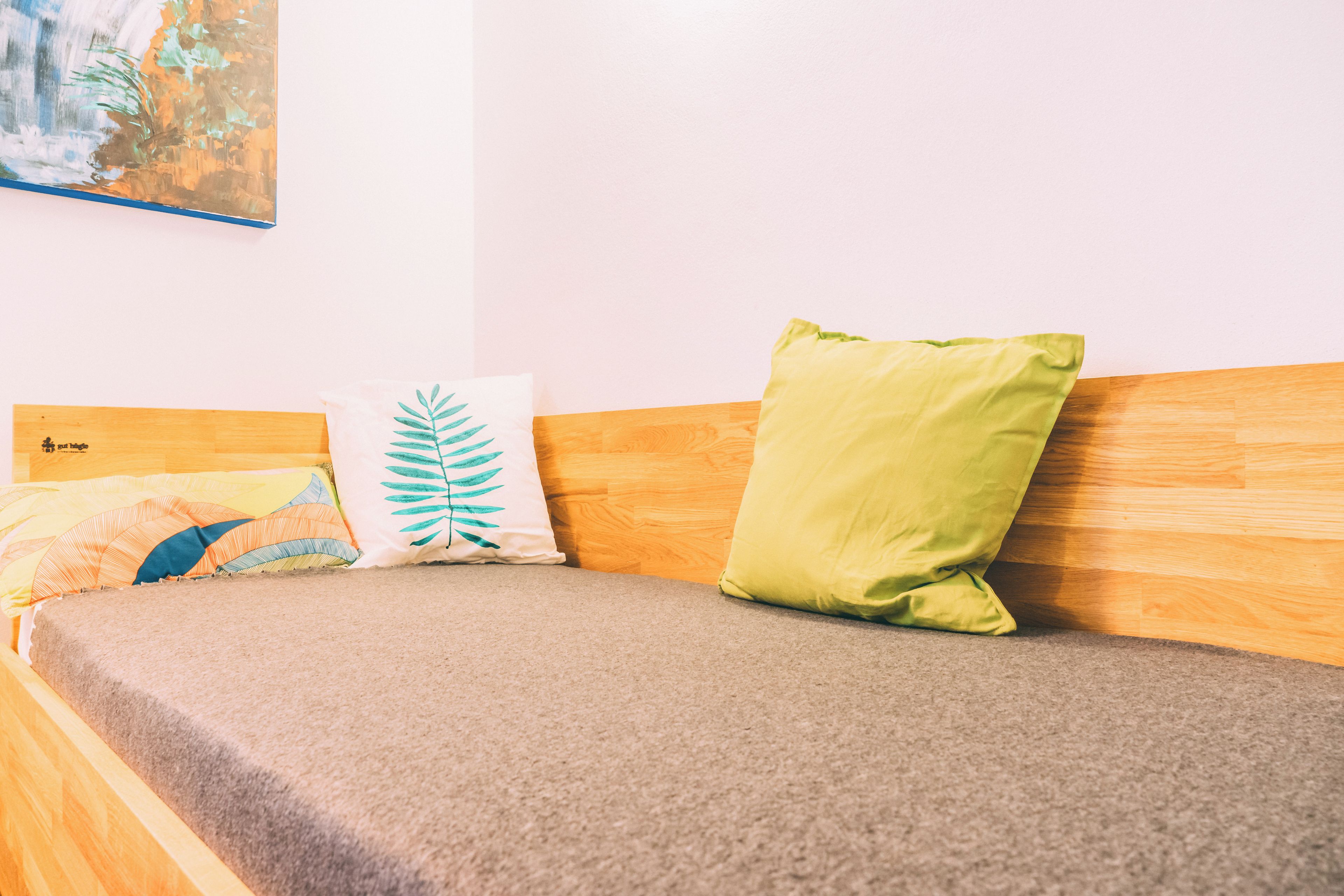 A bed with a wooden headboard, a grey mattress, and three pillows with different patterns.